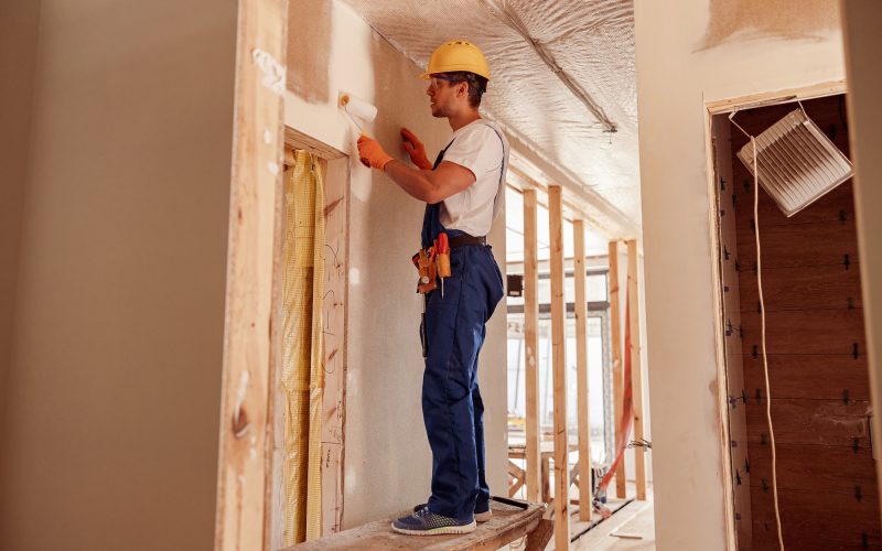 Male builder painting wall in house under construction